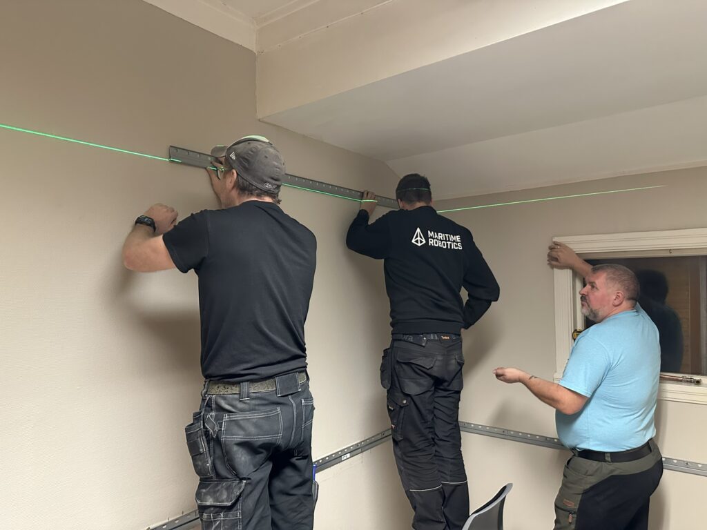 Kristian, Terje og Jan Erling henger opp skinne til kjøkkenskap